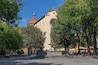 A historic church with a dome and bell tower, surrounded by trees and a fountain in a public square.