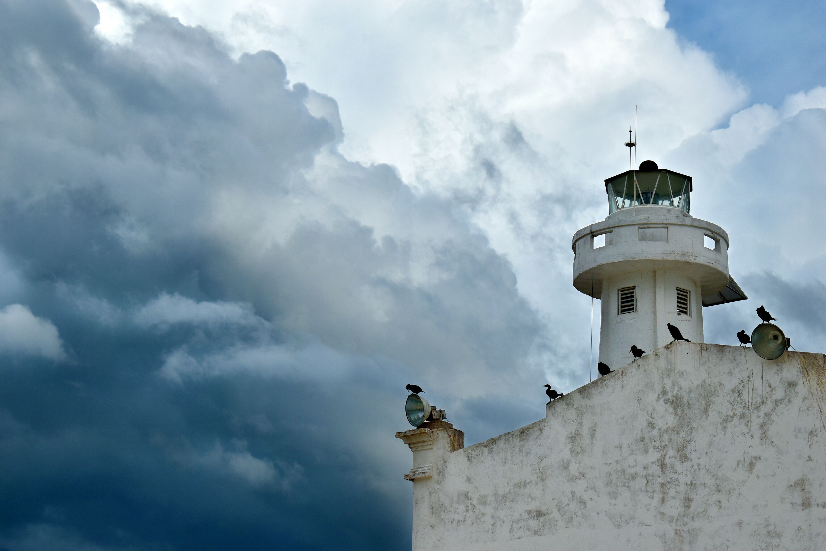 A lighthouse on an old building in Telchac Puerto on the coast of Yucatán on the Gulf of Mexico, cormorants sitting on the roof, big storm clouds in the background