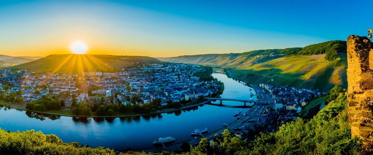 A river winding through a town with a bridge, surrounded by hills and a stone wall.