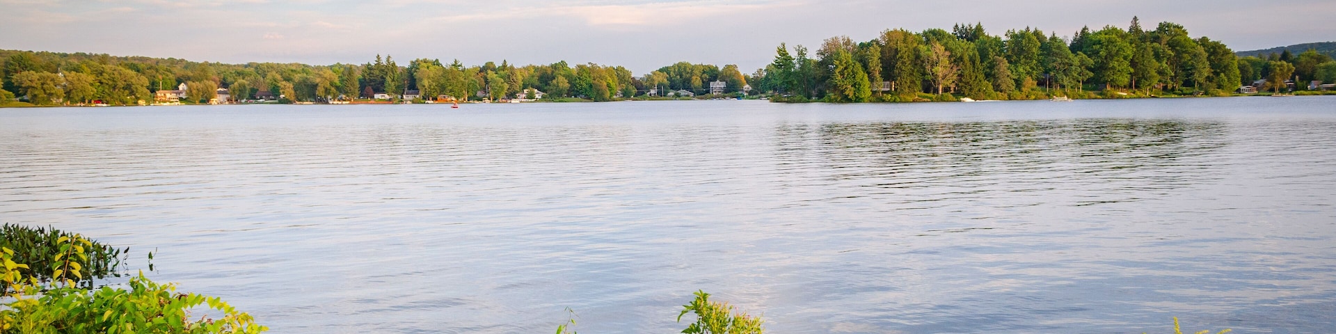 Um lago calmo com margens arborizadas e céu claro.