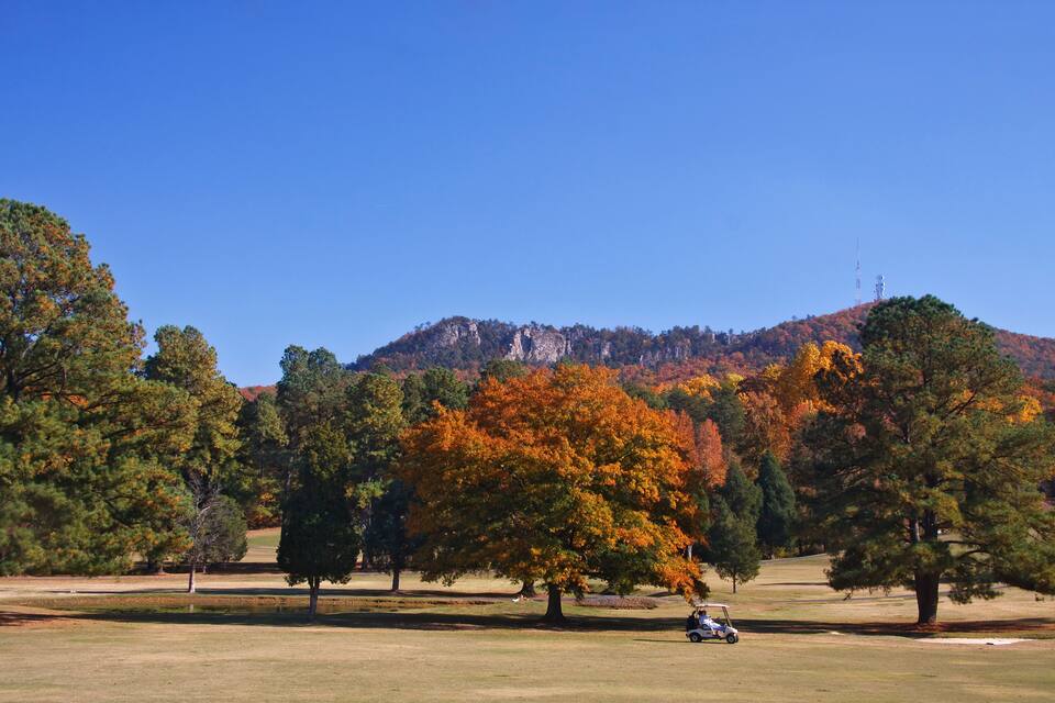 A golf course with autumn-colored trees and a mountain in the background.
