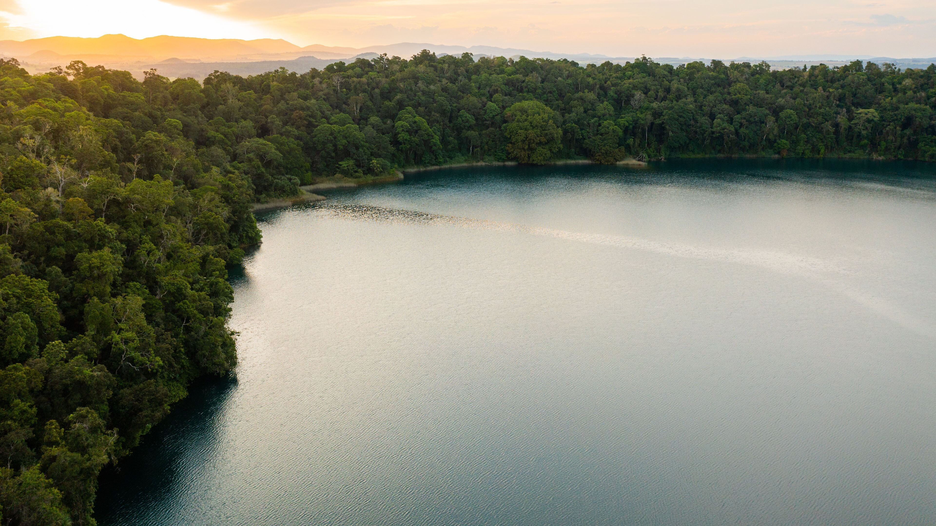 A large lake surrounded by dense forest and distant mountains.