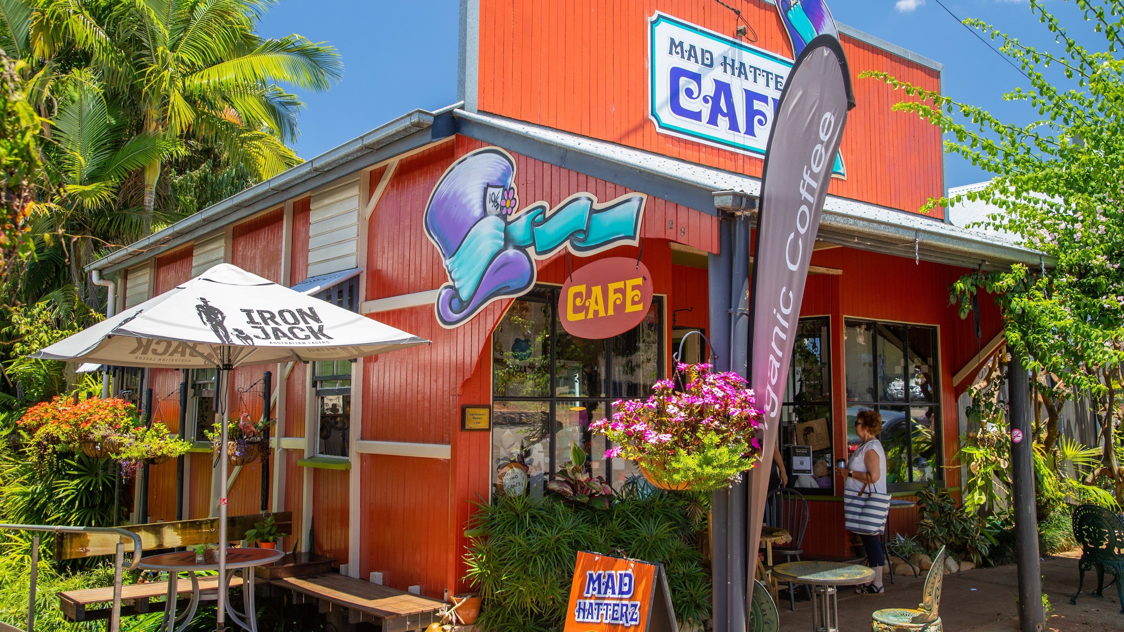 A red building with a cafe sign, outdoor seating, and a 'Mad Hatters Cafe' sign.