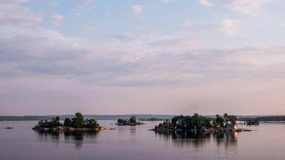 A calm lake with several small islands, some with trees and buildings, under a partly cloudy sky.