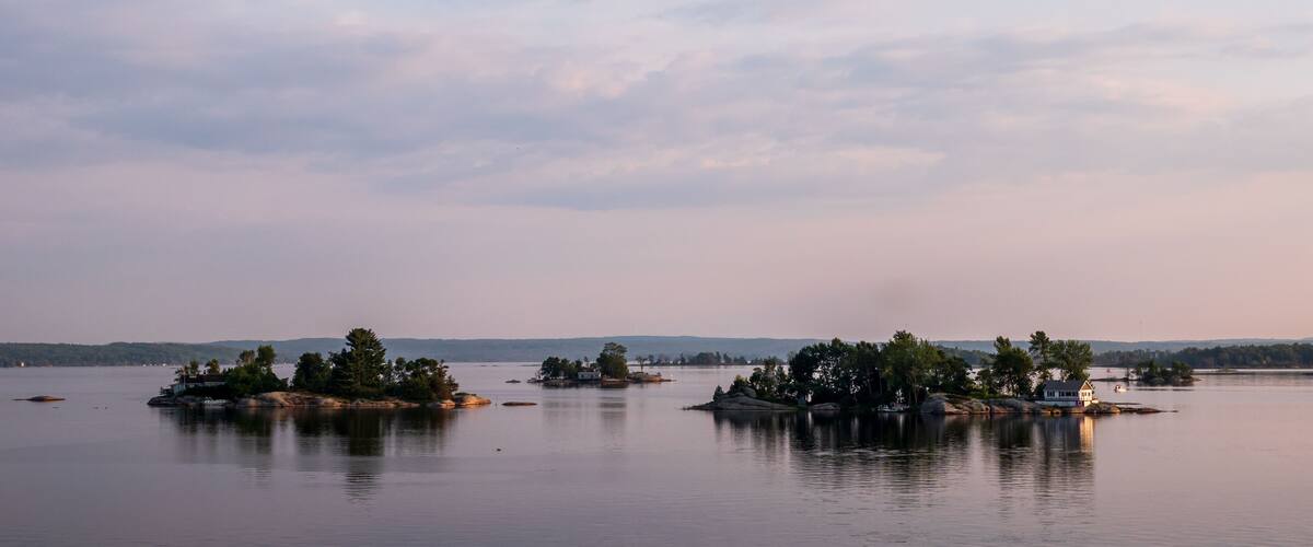 A calm lake with several small islands, some with trees and buildings, under a partly cloudy sky.