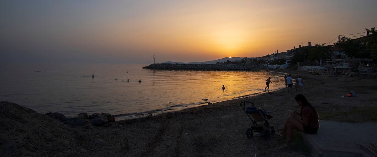 A beach at sunset with people swimming and walking along the shore.