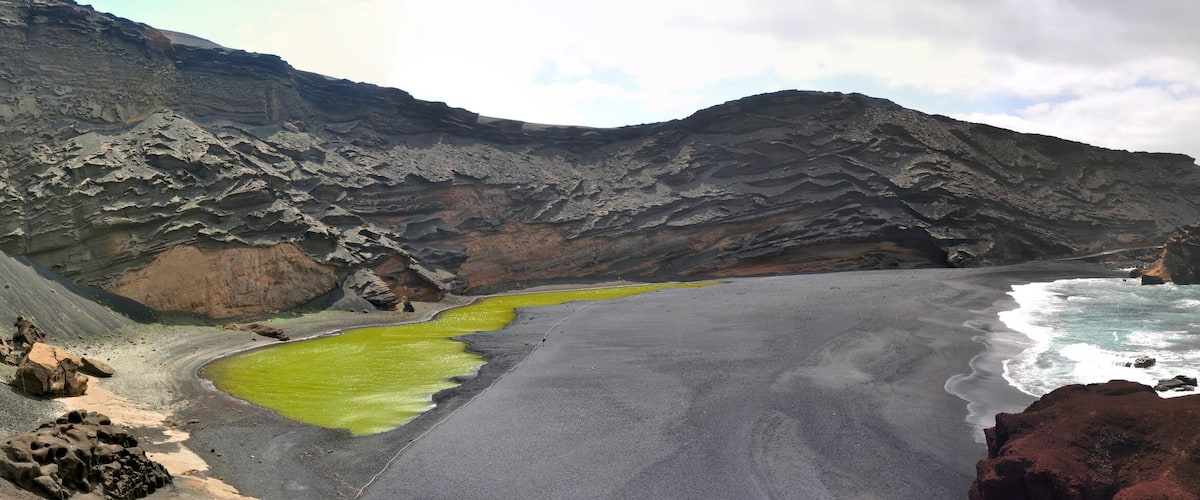 A coastal landscape with a green lagoon, a sandy beach, and rocky cliffs.