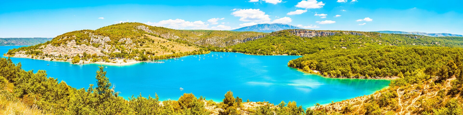 Un paisaje costero con una bahía turquesa, colinas verdes y un pueblo en la ladera.