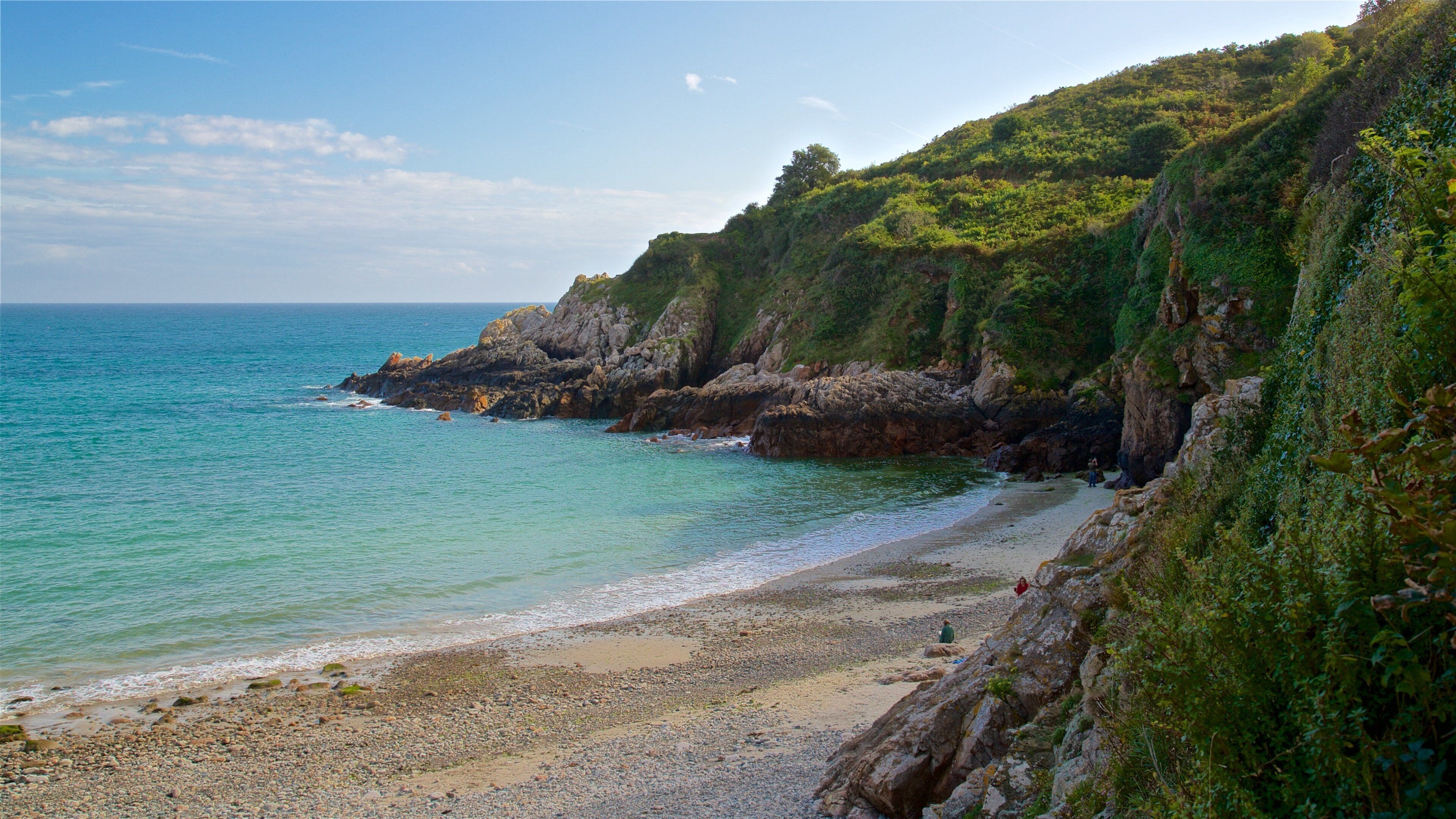A rocky coastline with a pebbly beach and lush green cliffs.