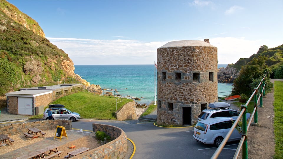 A coastal road with a stone tower, picnic tables, and parked cars.