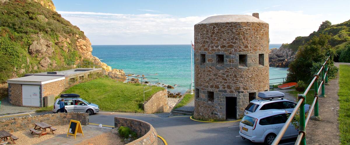 A coastal road with a stone tower, picnic tables, and parked cars.