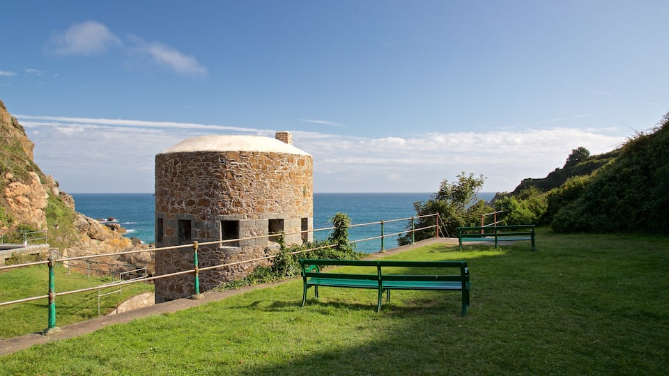 A stone tower by the sea, a grassy area, and a bench.