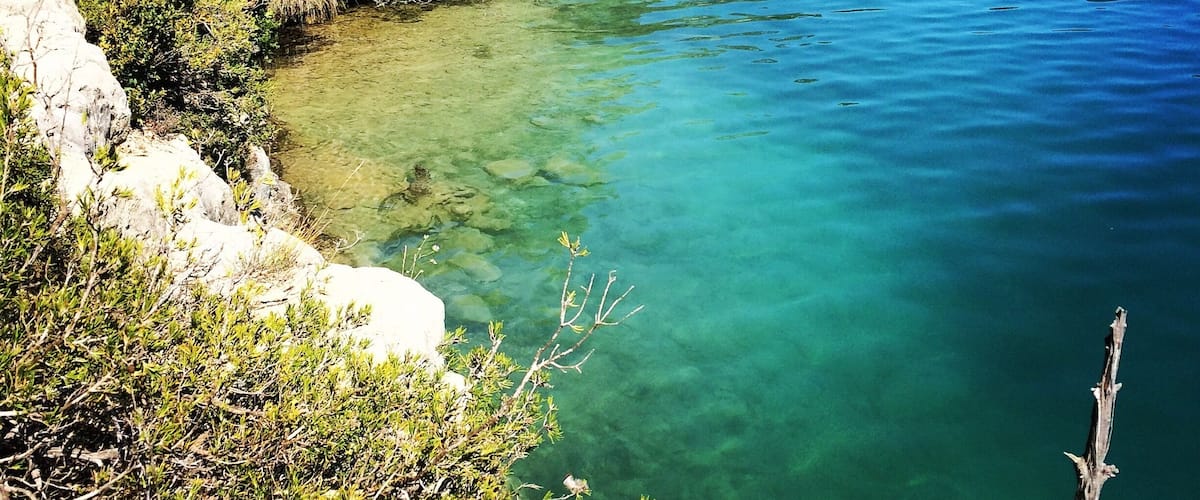 A clear blue river surrounded by dense greenery and rocky terrain.