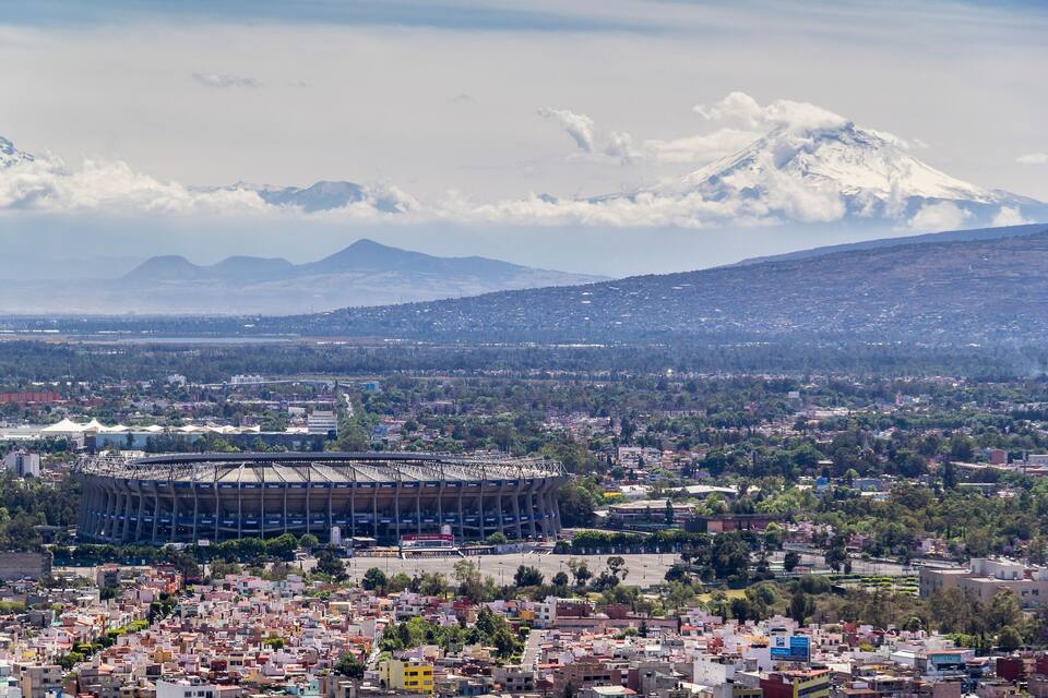 A cityscape with a large stadium, a snow-capped mountain, and a densely populated area.