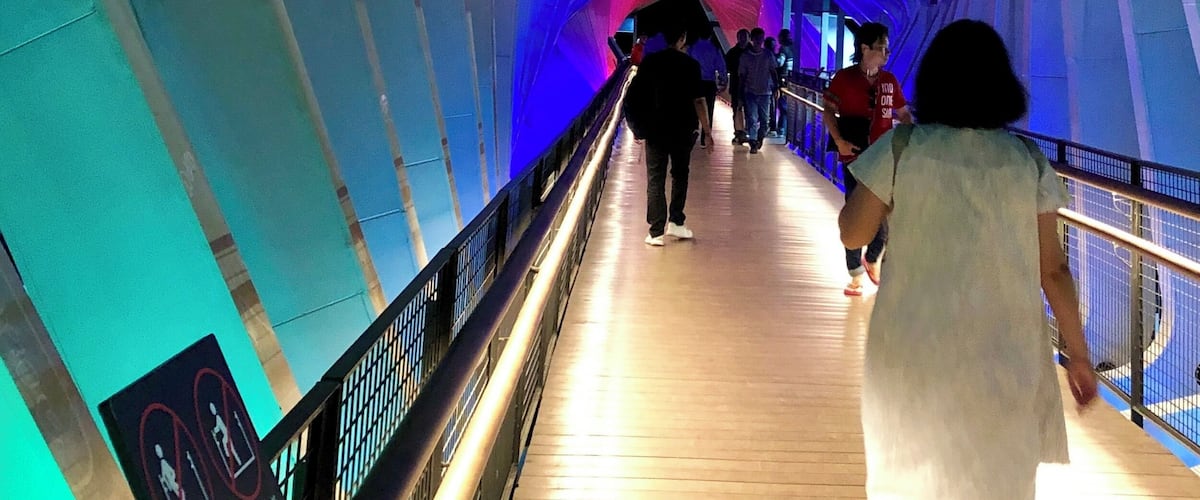 A pedestrian bridge with a curved design and illuminated blue and white lights.
