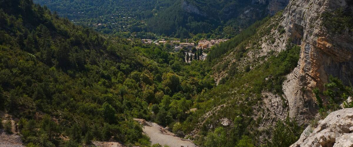 A mountainous landscape with a village nestled in the valley, surrounded by dense forests and rocky cliffs.