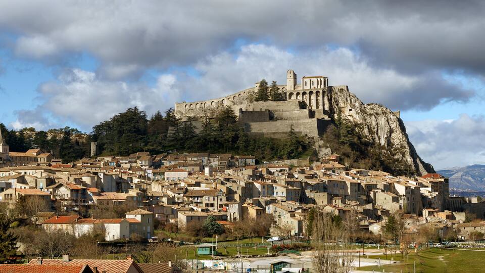 A historic town with a prominent church on a hill, surrounded by mountains and a river.