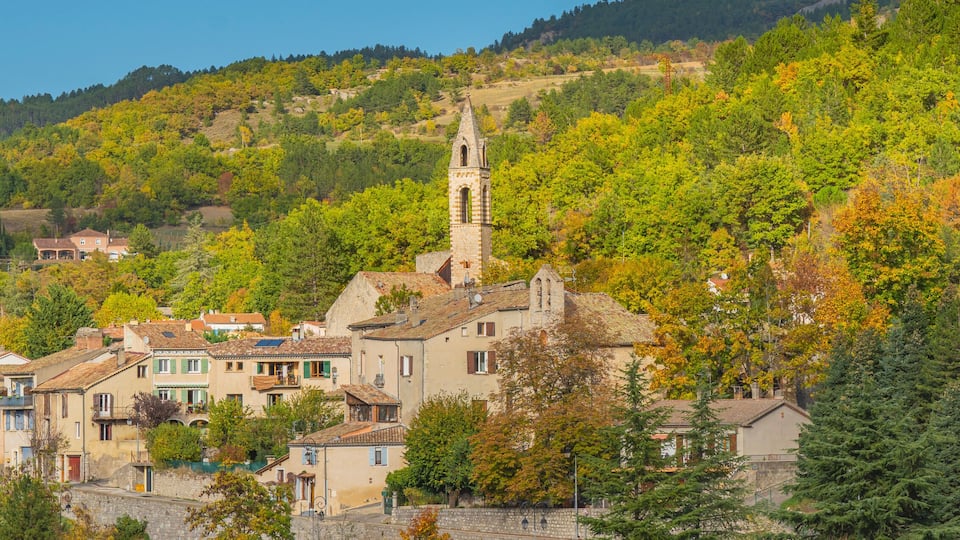A hillside village with a church tower, surrounded by autumn-colored trees and traditional buildings.