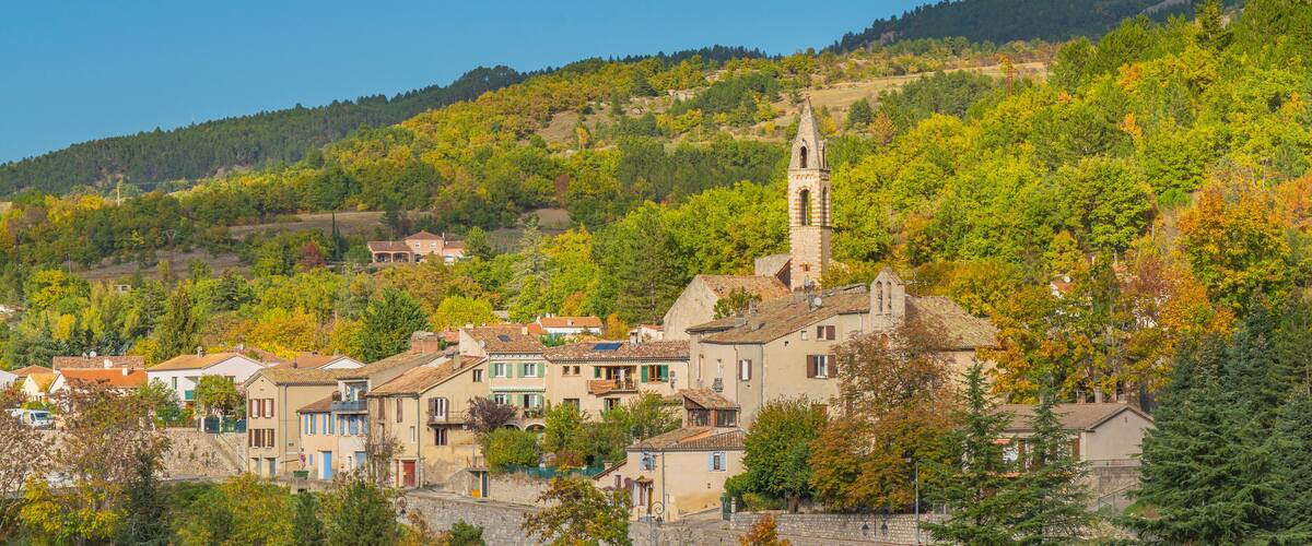 A hillside village with a church tower, surrounded by autumn-colored trees and traditional buildings.