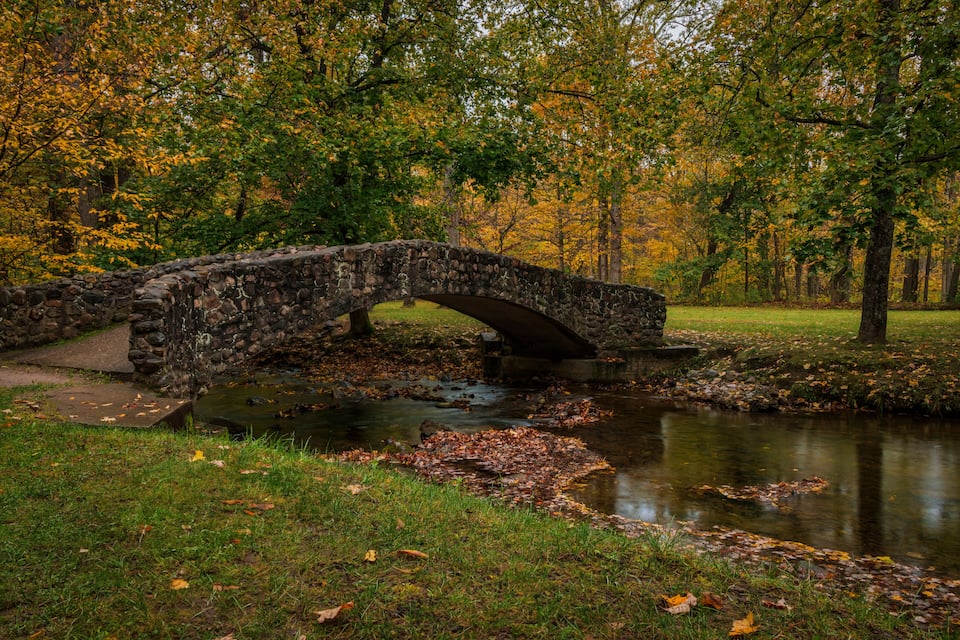 Un puente de piedra sobre un arroyo en un parque con follaje otoñal.