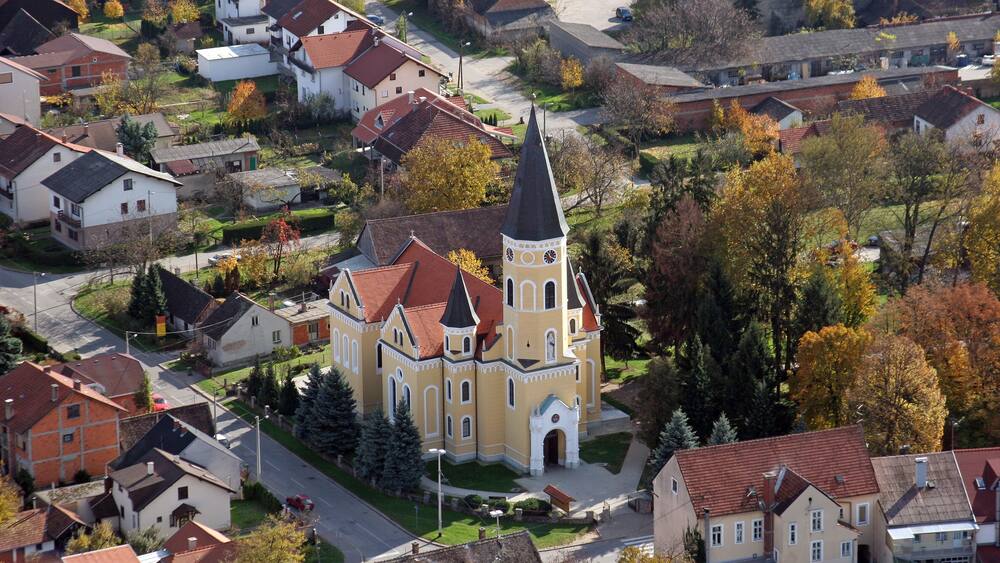 A church with a tall spire, surrounded by residential houses and autumn foliage.