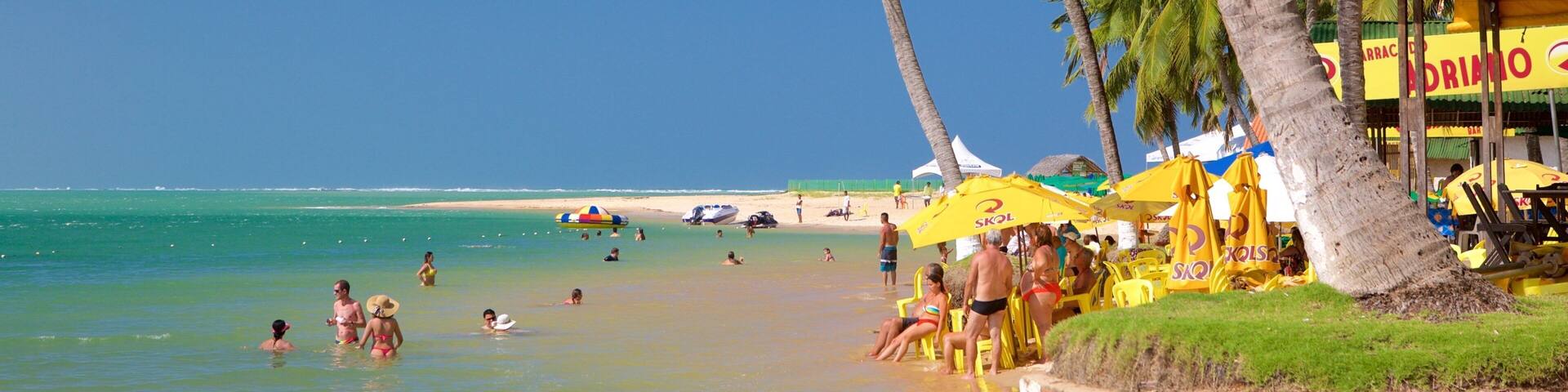 A beach with palm trees, people swimming, and yellow umbrellas.
