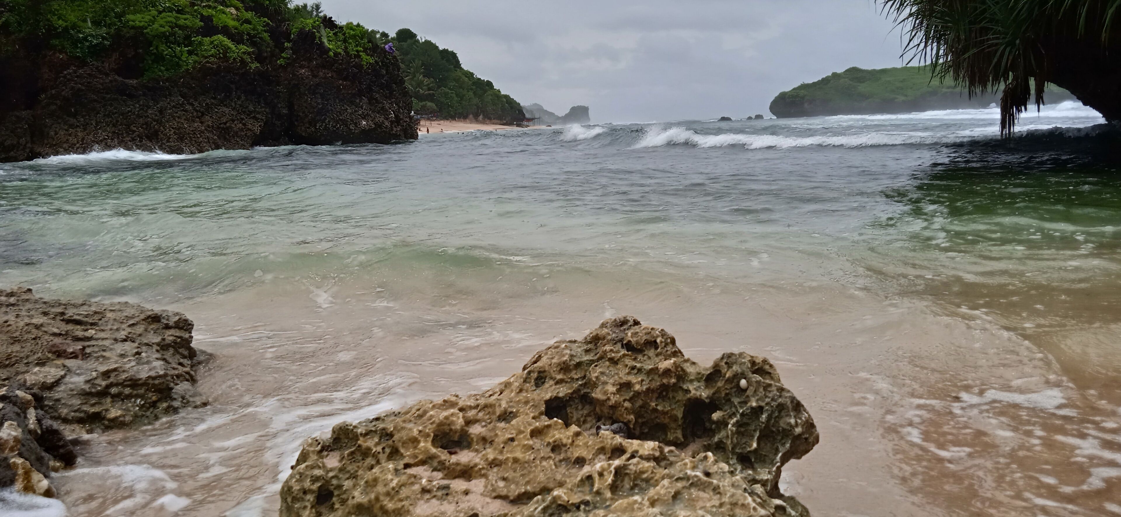 A rocky beach with clear water, a distant shoreline, and lush greenery.