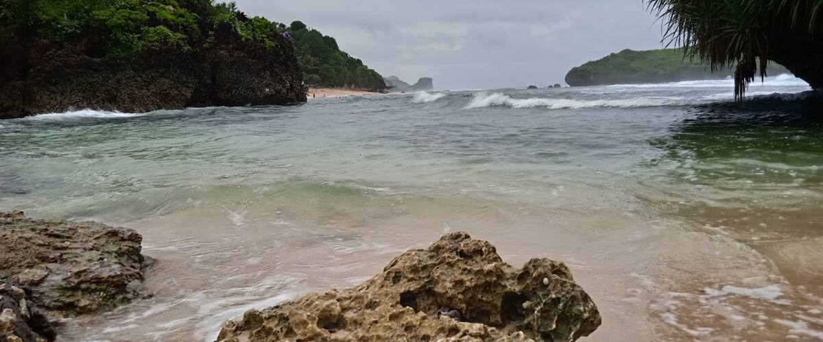 A rocky beach with clear water, a distant shoreline, and lush greenery.