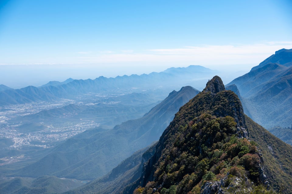 Cordillera montañosa con un pico destacado, un valle en la parte baja y una ciudad lejana.
