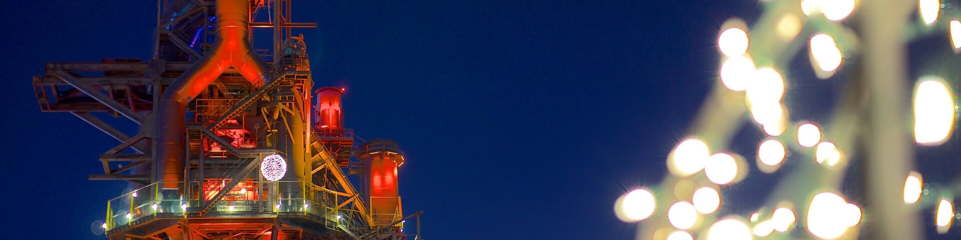 Instalación industrial nocturna con estructuras iluminadas y luces esféricas.