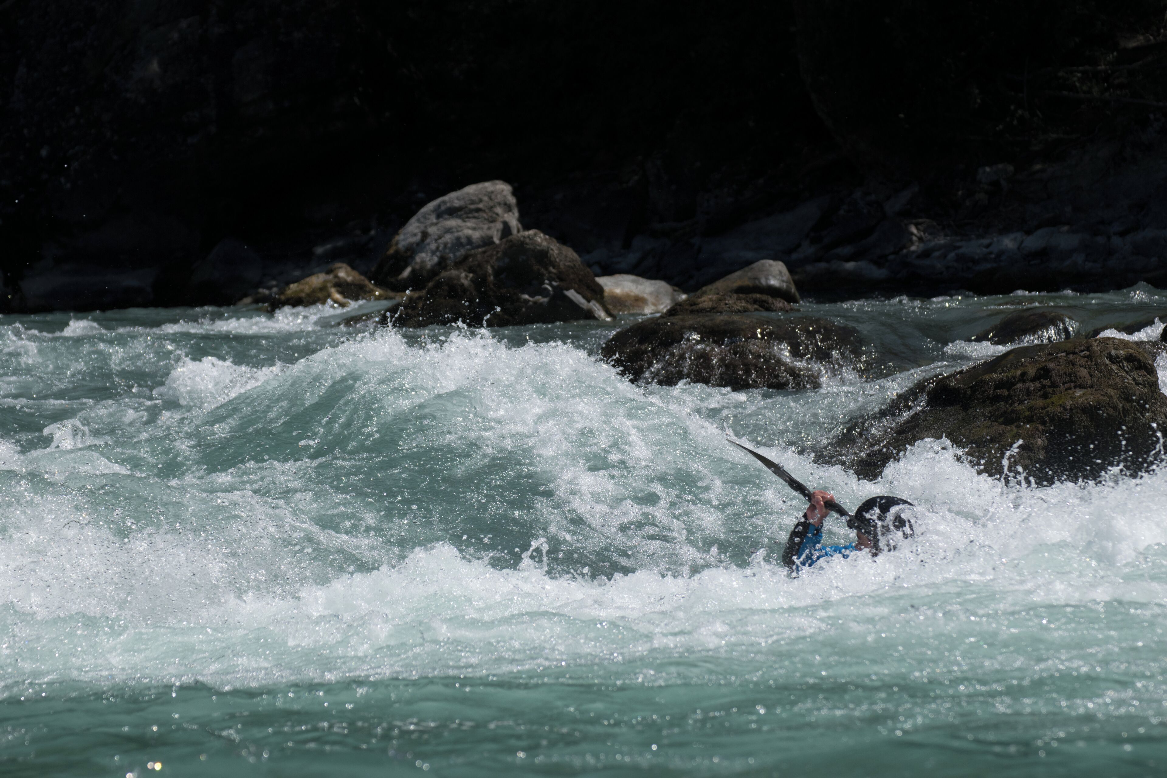 A kayaker navigating turbulent waters with large rocks in the background.