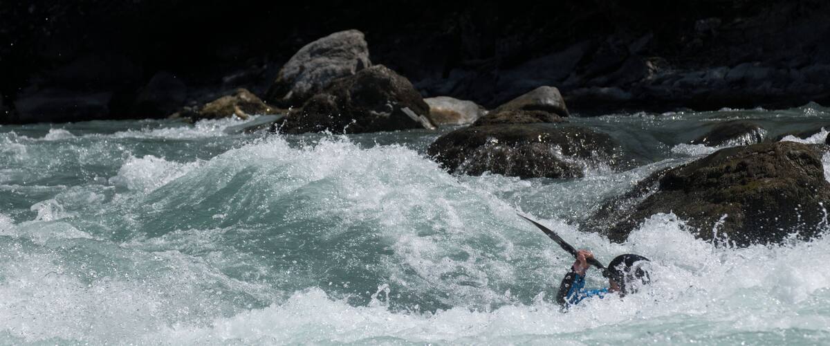A kayaker navigating turbulent waters with large rocks in the background.