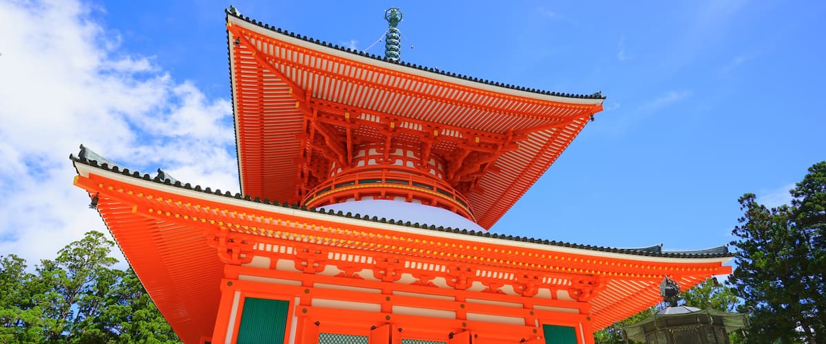 Een traditionele Japanse pagode met een felrood dak en groene accenten, tegen een helderblauwe lucht.