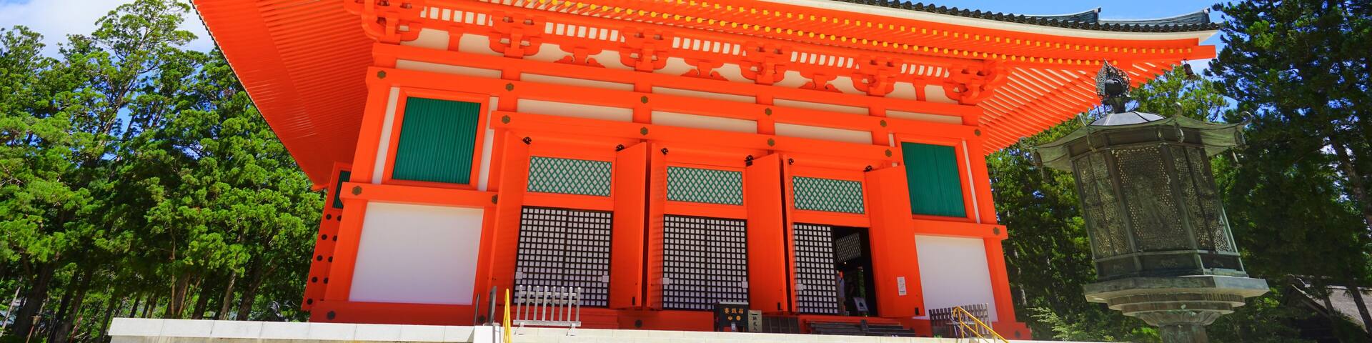 A traditional Japanese pagoda with a bright red roof and green accents, set against a clear blue sky.