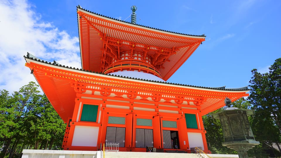 A traditional Japanese pagoda with a bright red roof and green accents, set against a clear blue sky.