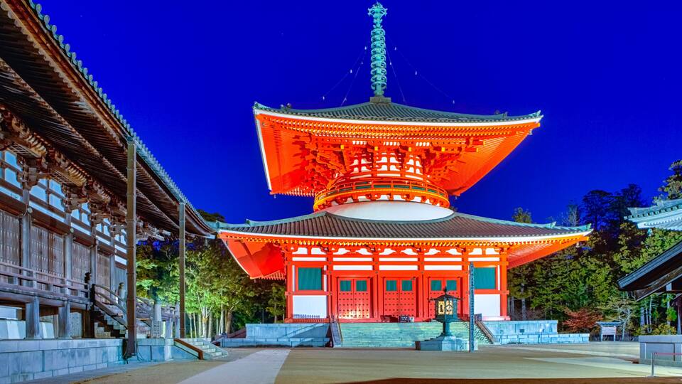 A traditional Japanese pagoda with a multi-tiered roof, illuminated by warm lights against a twilight sky.