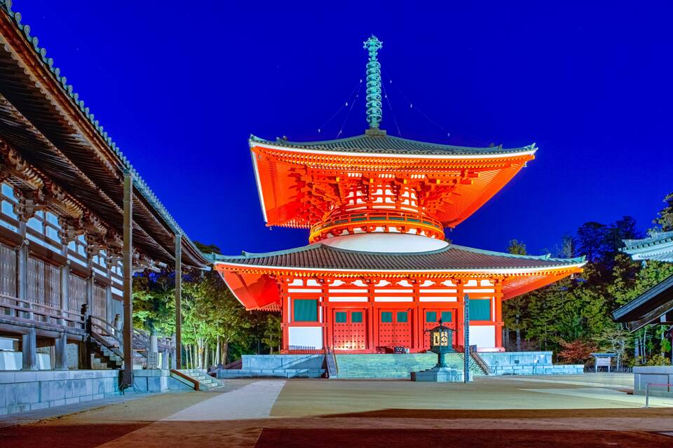 A traditional Japanese pagoda with a multi-tiered roof, illuminated by warm lights against a twilight sky.