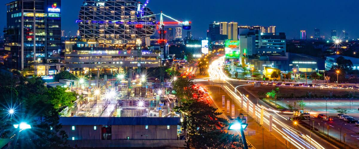 A cityscape at night with illuminated buildings, a prominent dome-shaped structure, and a busy highway with light trails.