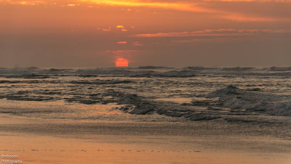 A sunset over the ocean with waves and a visible sun.