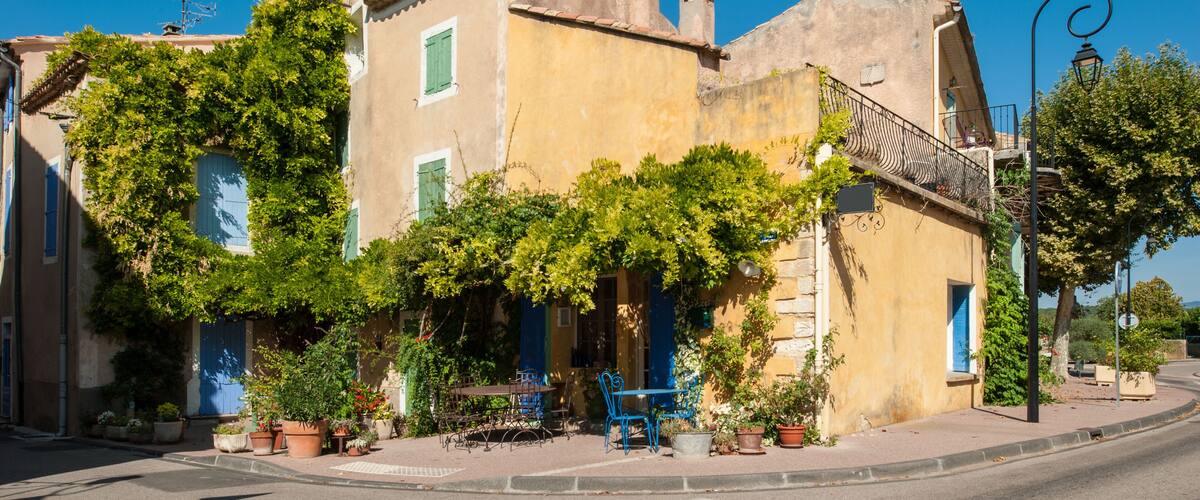 A historic building with ivy-covered walls, blue shutters, and outdoor seating.