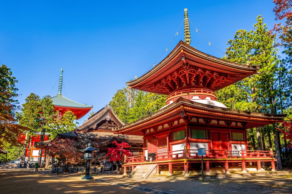 Un pagès japonès tradicional amb una combinació de colors vermell i blanc, envoltat d'arbres i un cel blau clar.