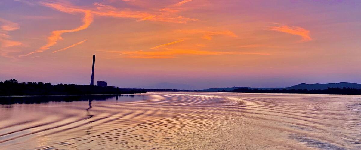 A sunset over a calm body of water with a distant mountain range and a tall structure on the left.