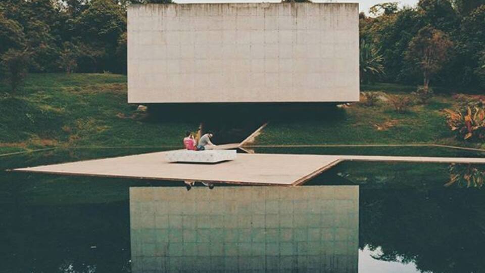 A large concrete structure with a flat roof, surrounded by a body of water and greenery.