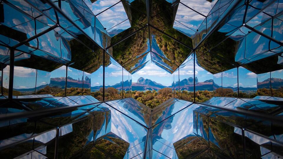 A symmetrical glass structure reflecting a mountainous landscape.