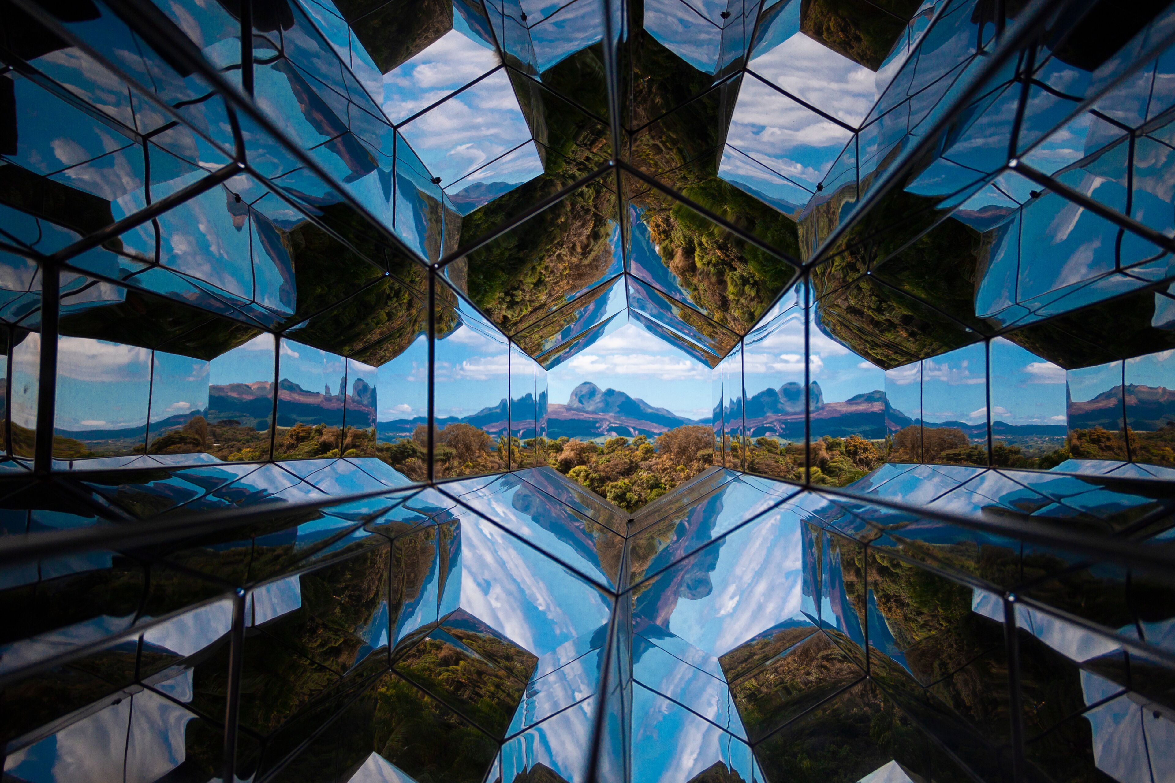 A symmetrical glass structure reflecting a mountainous landscape.