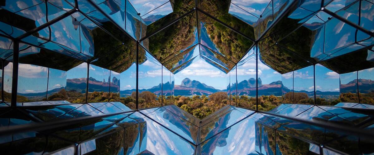 A symmetrical glass structure reflecting a mountainous landscape.