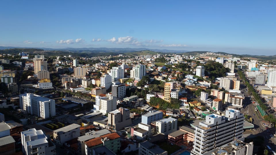 A cityscape with a mix of high-rise and low-rise buildings, a clear blue sky, and distant mountains.