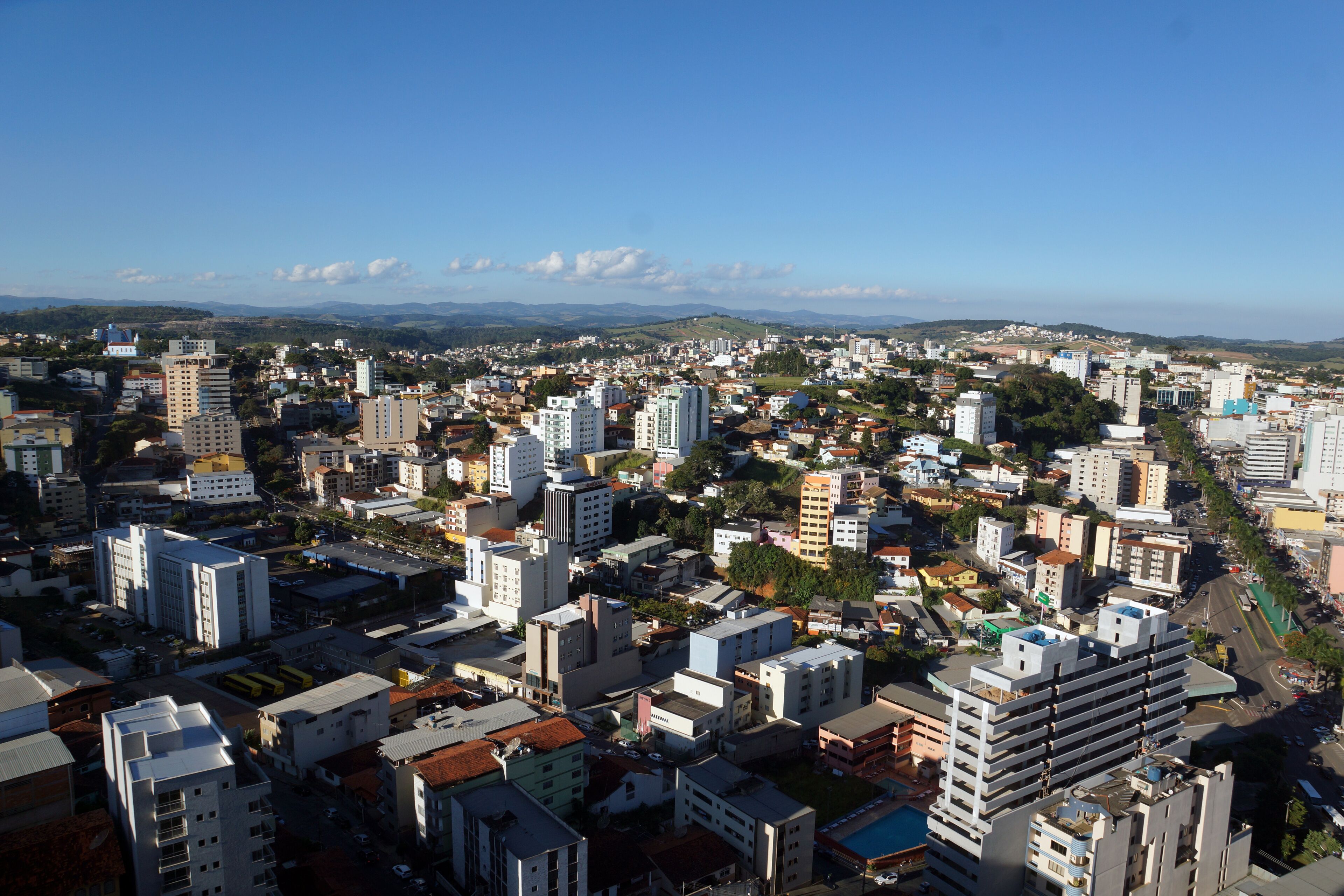 A cityscape with a mix of high-rise and low-rise buildings, a clear blue sky, and distant mountains.