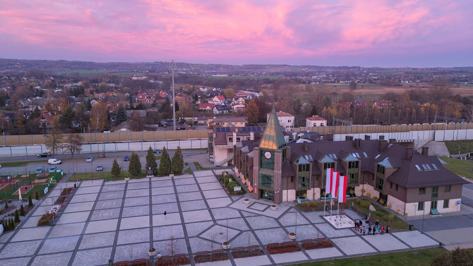 A town square with a clock tower, surrounded by residential buildings and a sports field.