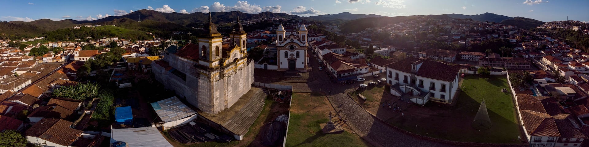 Aerial 360 degrees panorama of the central historical square with two churches in the colonial mining city of Mariana in Minas Gerais, Brazil, with one under renovation against a blue sky with clouds